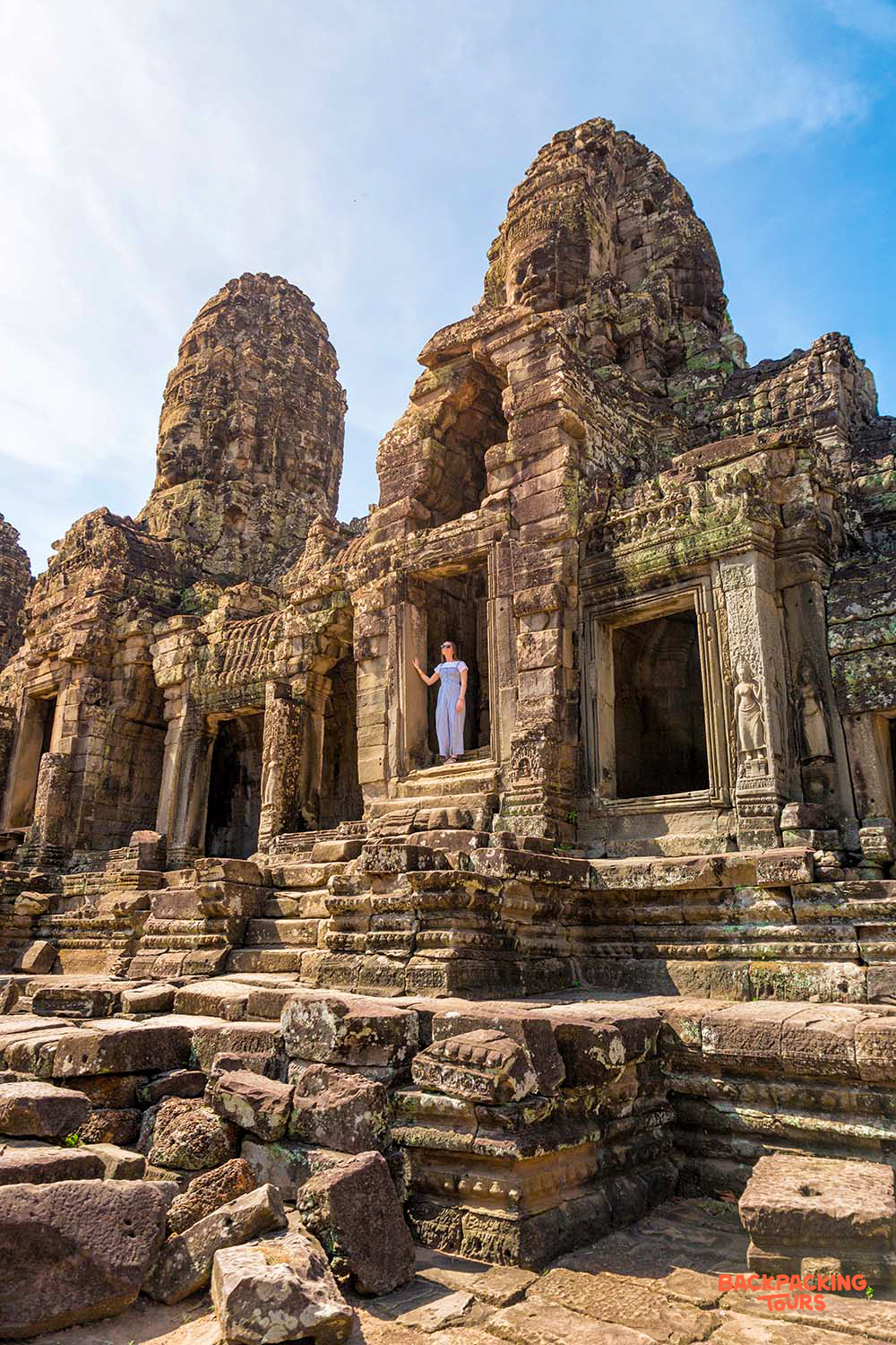 A woman stands in a doorway of an ancient temple, surrounded by the majestic stone faces of Angkor.