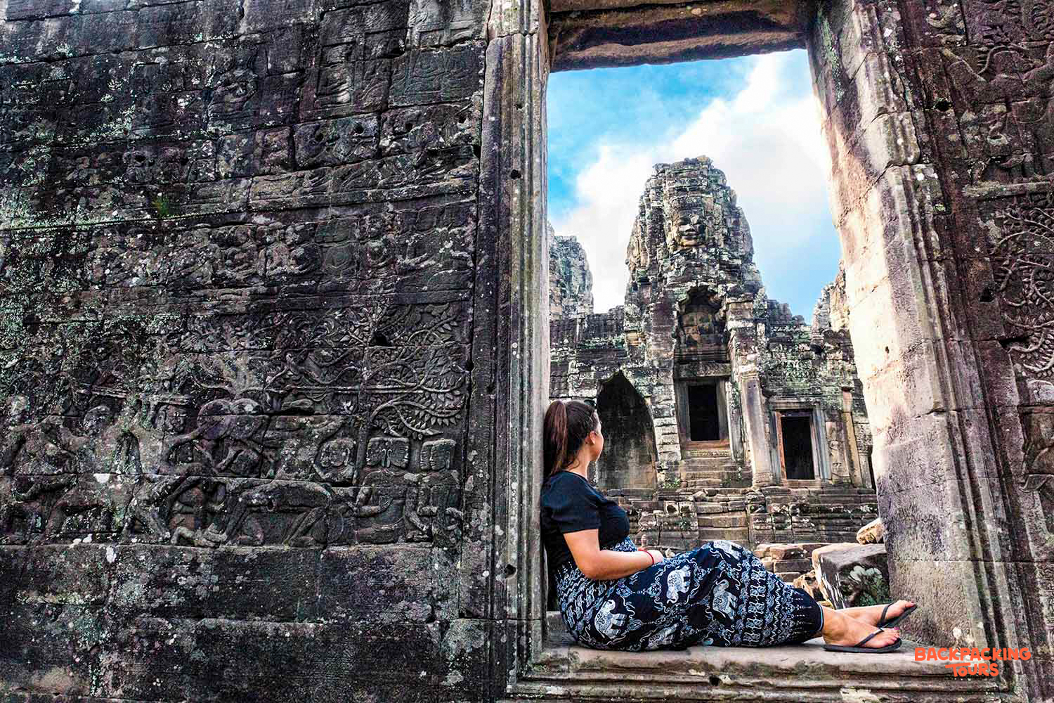 A woman sits in a stone doorway, looking out at the majestic Bayon Temple in Siem Reap.