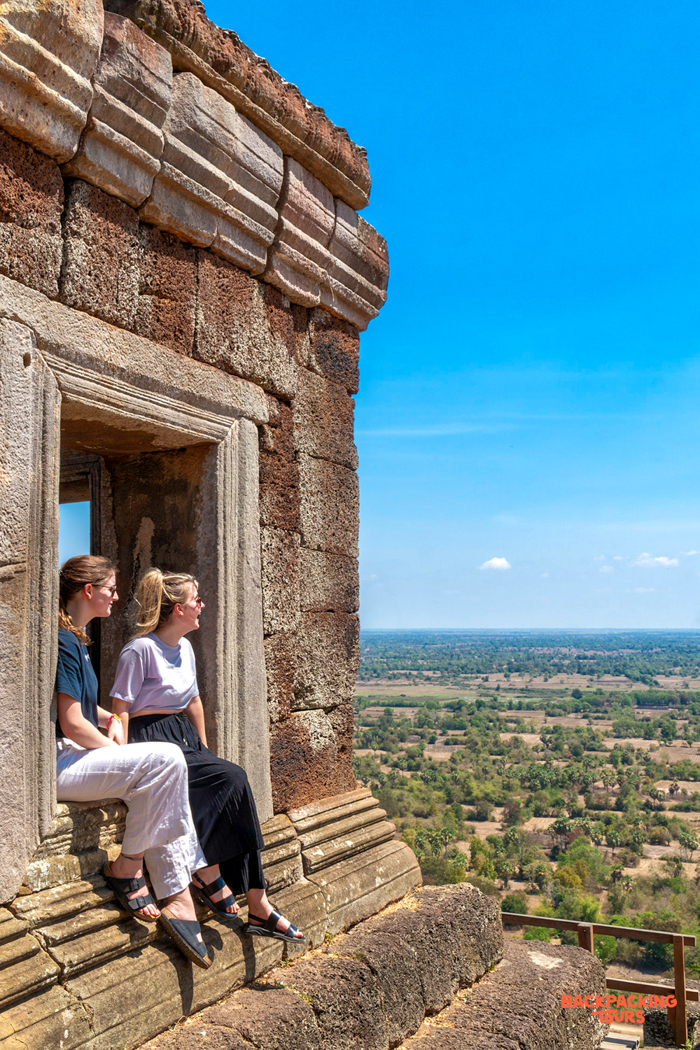 Friends relaxing in an ancient temple window, looking out over the expansive Siem Reap landscape.