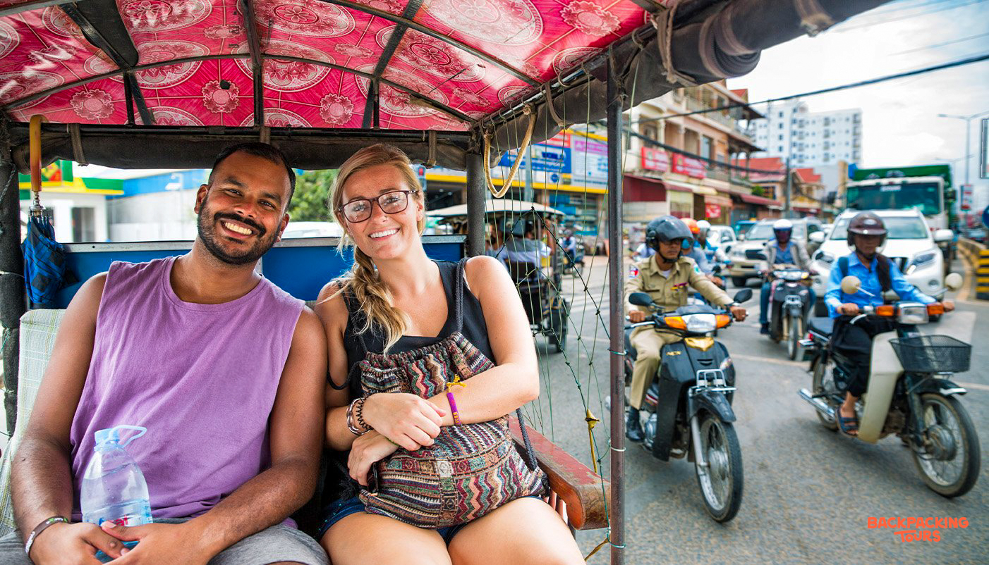 Two smiling travelers enjoying a tuk-tuk ride through the bustling streets of Phnom Penh.