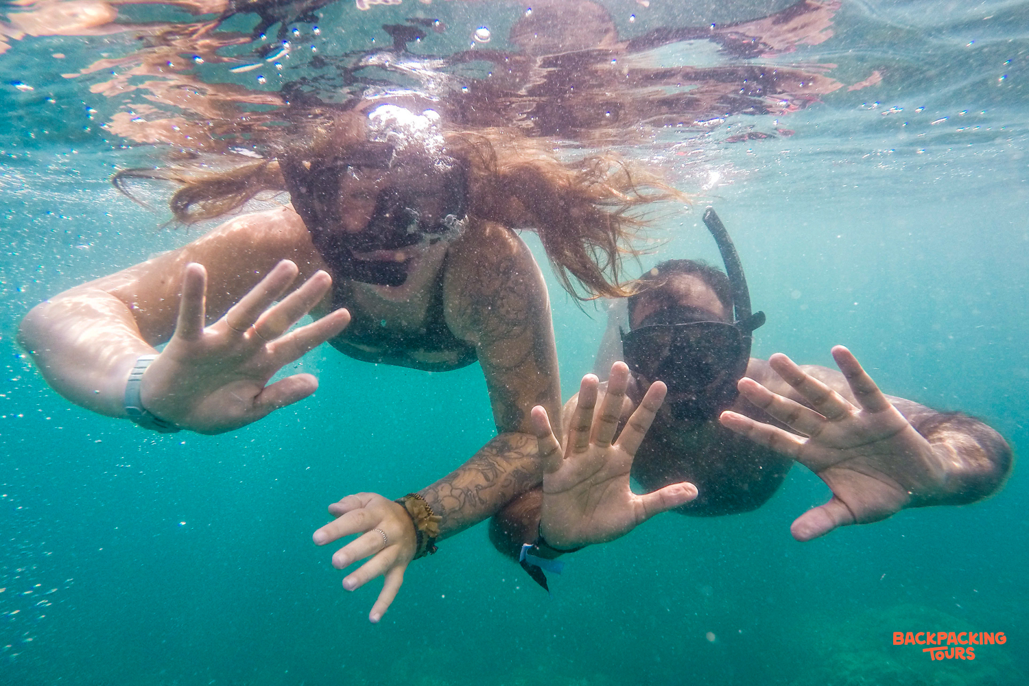 Two backpackers snorkel playfully underwater in the clear turquoise waters of Koh Rong, Cambodia.