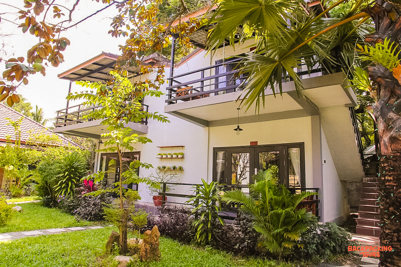 Peaceful two-story guesthouse with balconies, surrounded by lush tropical plants and a green lawn in Kampot.