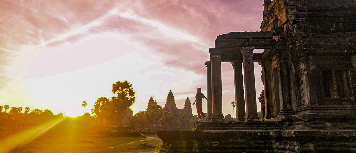 A traveler stands on ancient Angkor Wat temple ruins, silhouetted against a stunning golden sunrise.