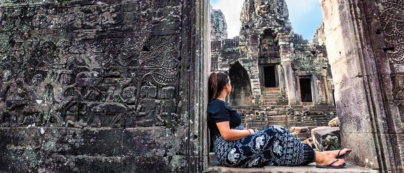 Woman sits contemplatively, admiring the ancient stone carvings and towering structures of Bayon Temple.