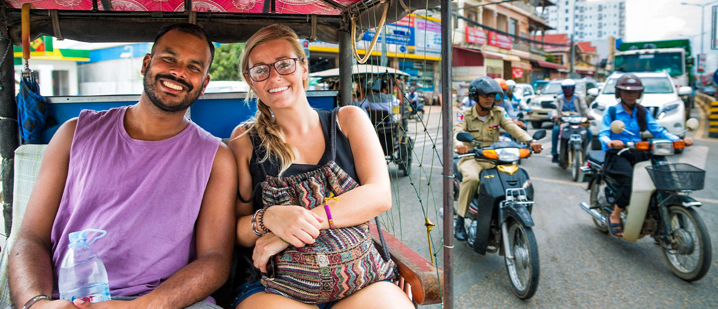 Smiling man and woman enjoying a tuk-tuk ride through the bustling streets of Phnom Penh.