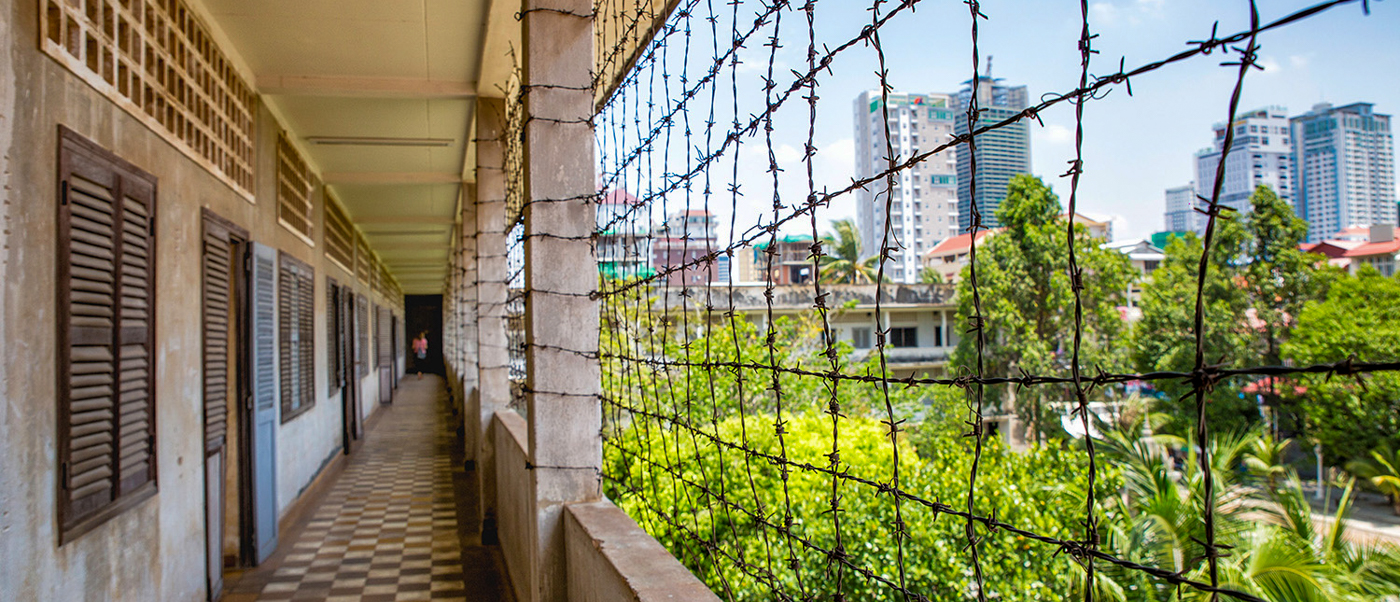 A long, stark corridor with barbed wire fencing overlooking the Phnom Penh city skyline.