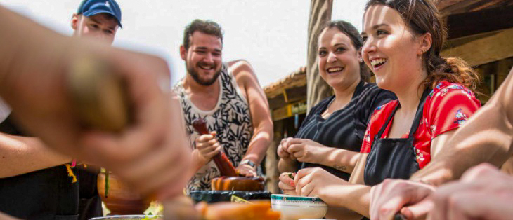Happy travelers learning to cook Cambodian dishes outdoors in Kampot, using mortars and pestles.