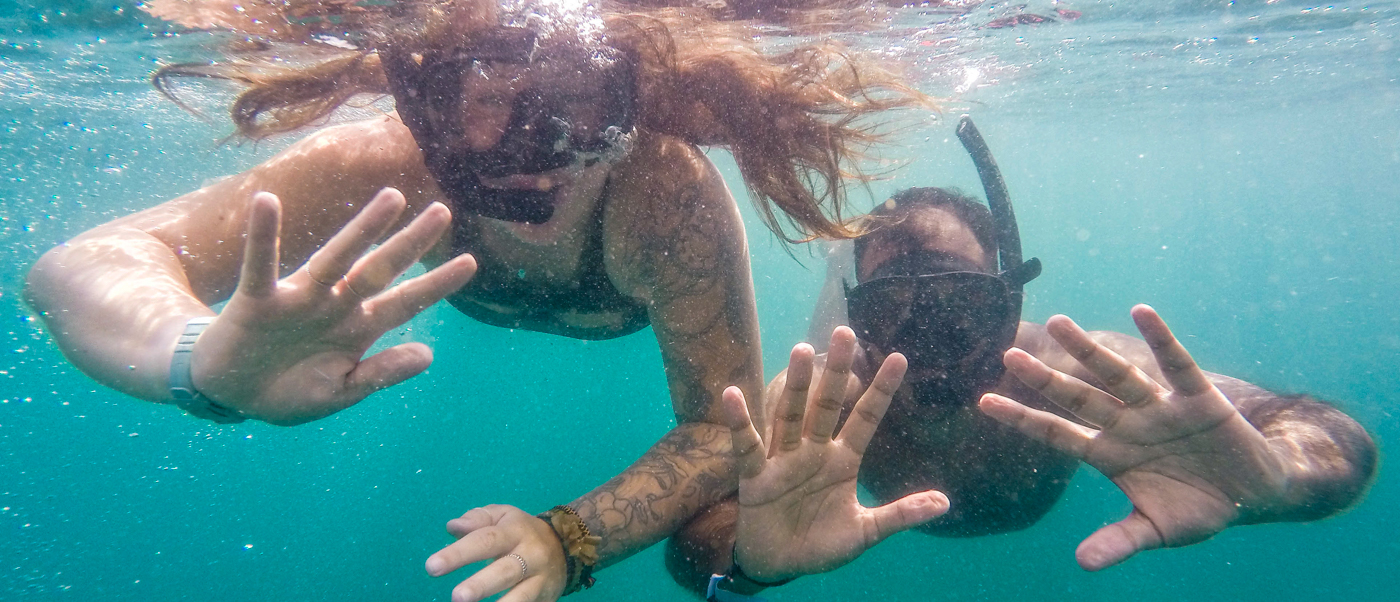 Two people wearing masks and snorkels swim playfully underwater in the clear Koh Rong sea.