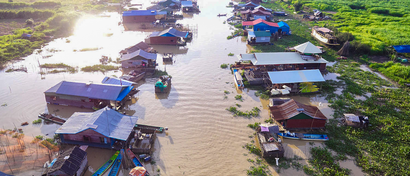 Traditional floating village with houses and boats on a wide, sunlit river in Siem Reap.