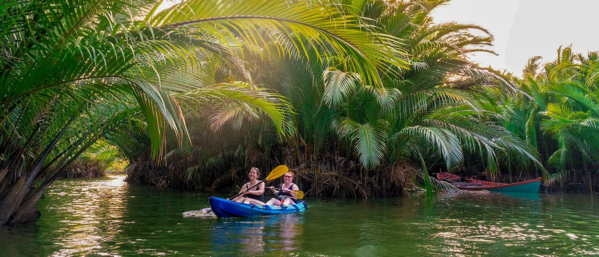 Two people kayaking on a tranquil river surrounded by lush green palm trees in Kampot.