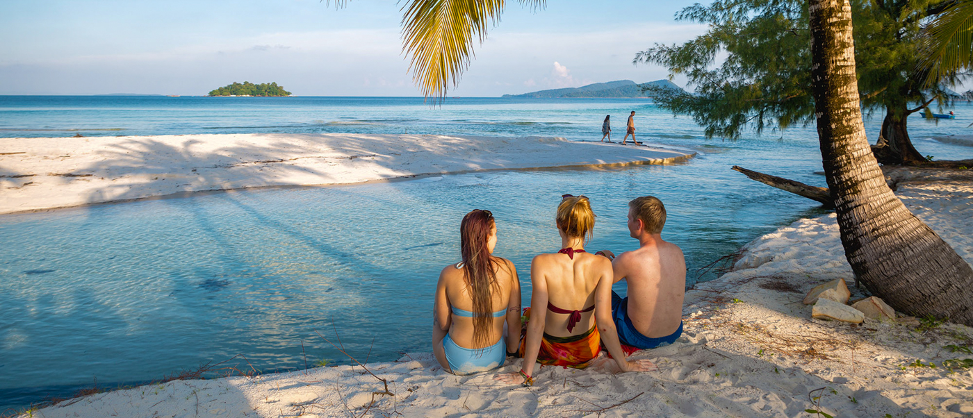 Three friends relax on a white sandy beach, watching the clear turquoise ocean in Koh Rong.