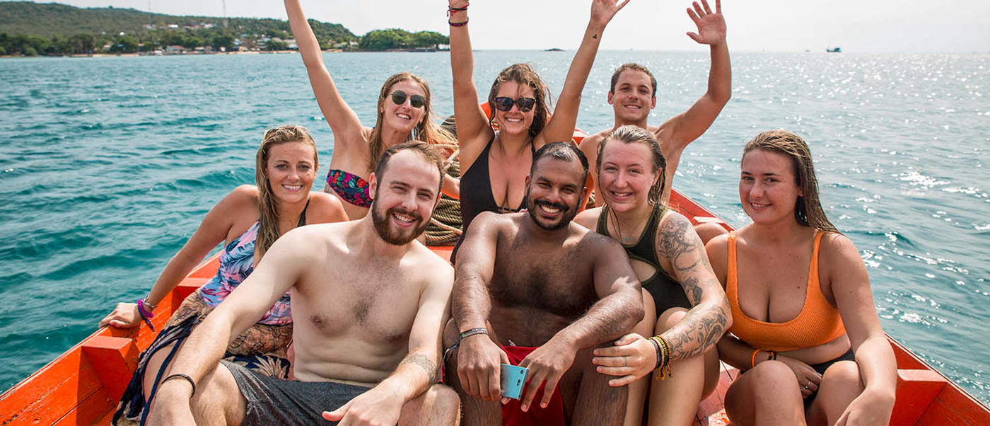 A group of happy friends on a boat trip in Koh Rong, smiling and waving.