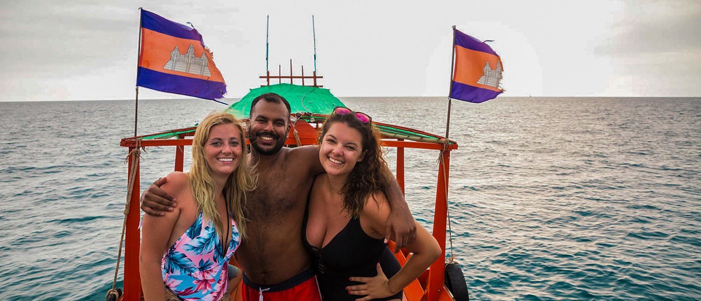 Three happy backpackers pose on a long-tail boat on the ocean in Koh Rong, Cambodia.
