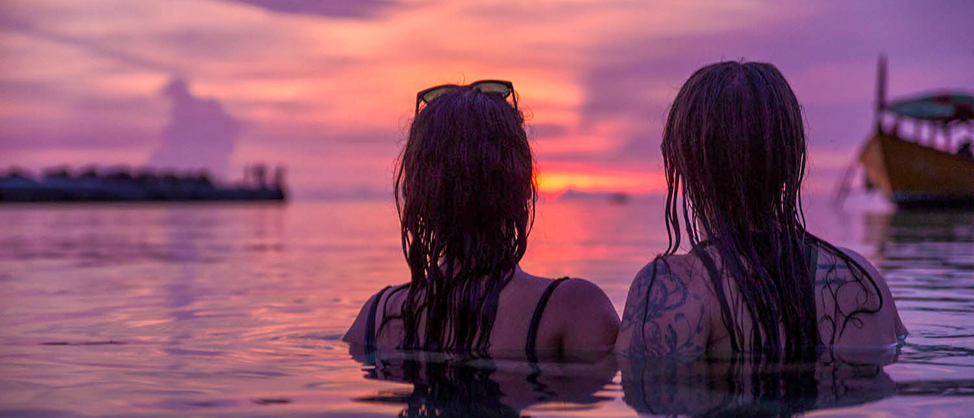 Two travelers relax in the warm ocean water, watching a beautiful purple sunset in Koh Rong.