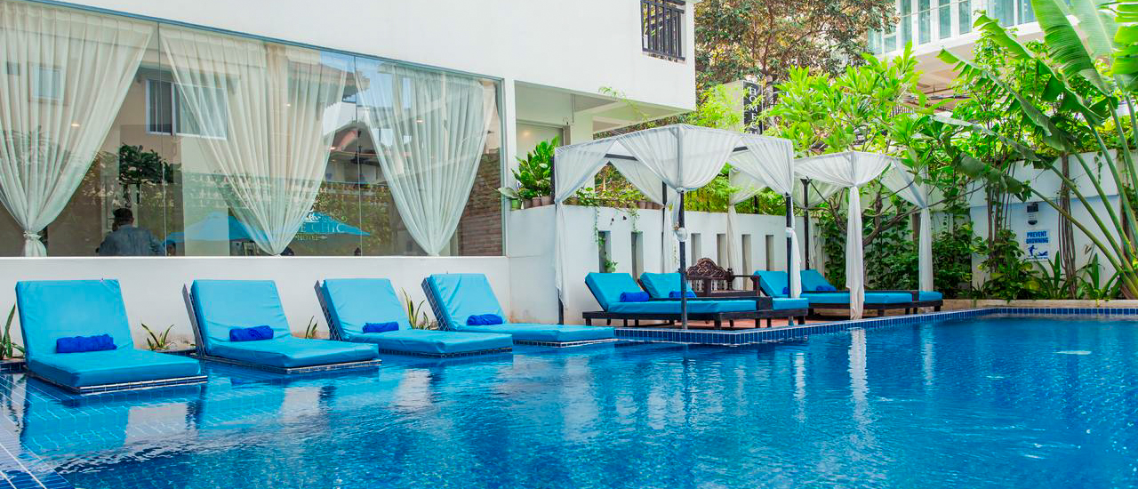 Bright blue swimming pool with submerged lounge chairs and shaded cabanas at a hotel in Phnom Penh.