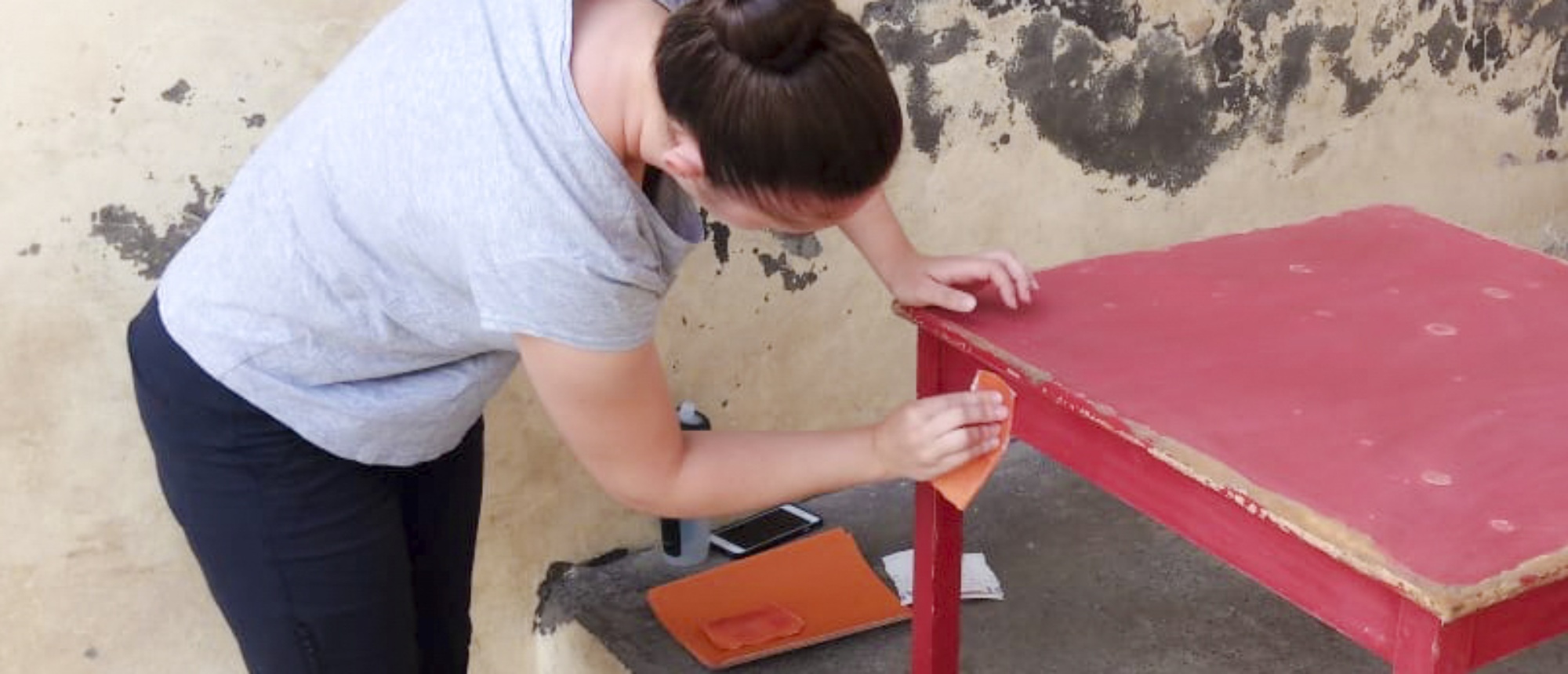 A volunteer sands a red table, preparing it for painting as part of a renovation project.