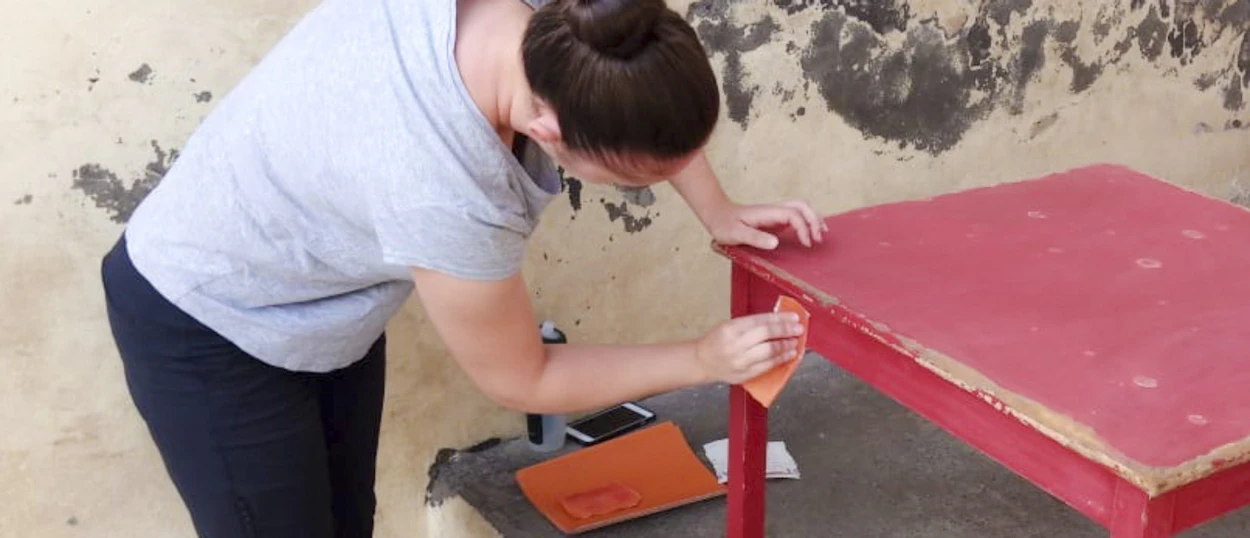 A volunteer sands a red table, preparing it for painting as part of a renovation project.