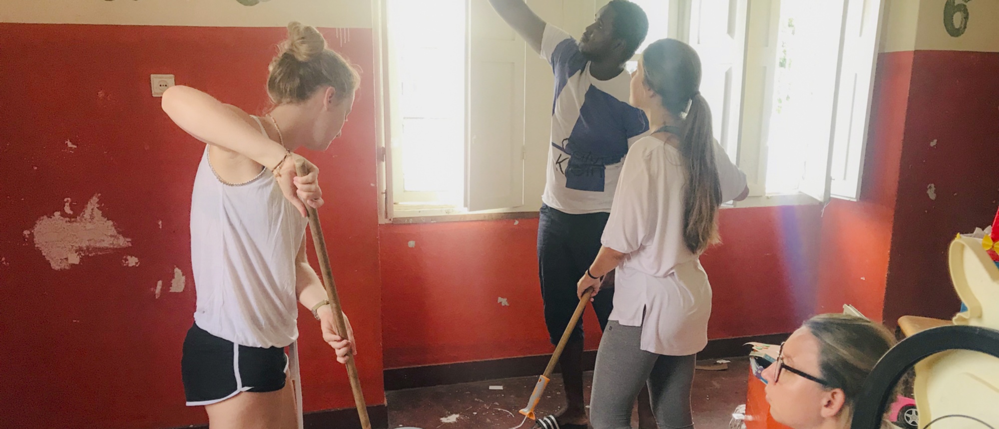 Three volunteers sweeping debris from a red-walled room during a renovation project.