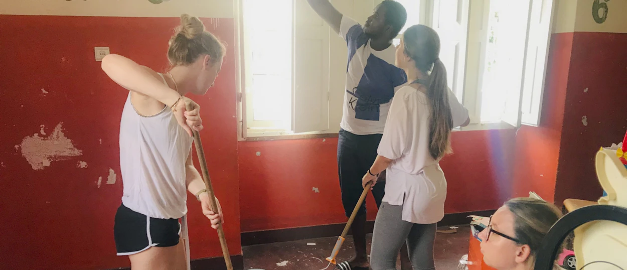 Three volunteers sweeping debris from a red-walled room during a renovation project.