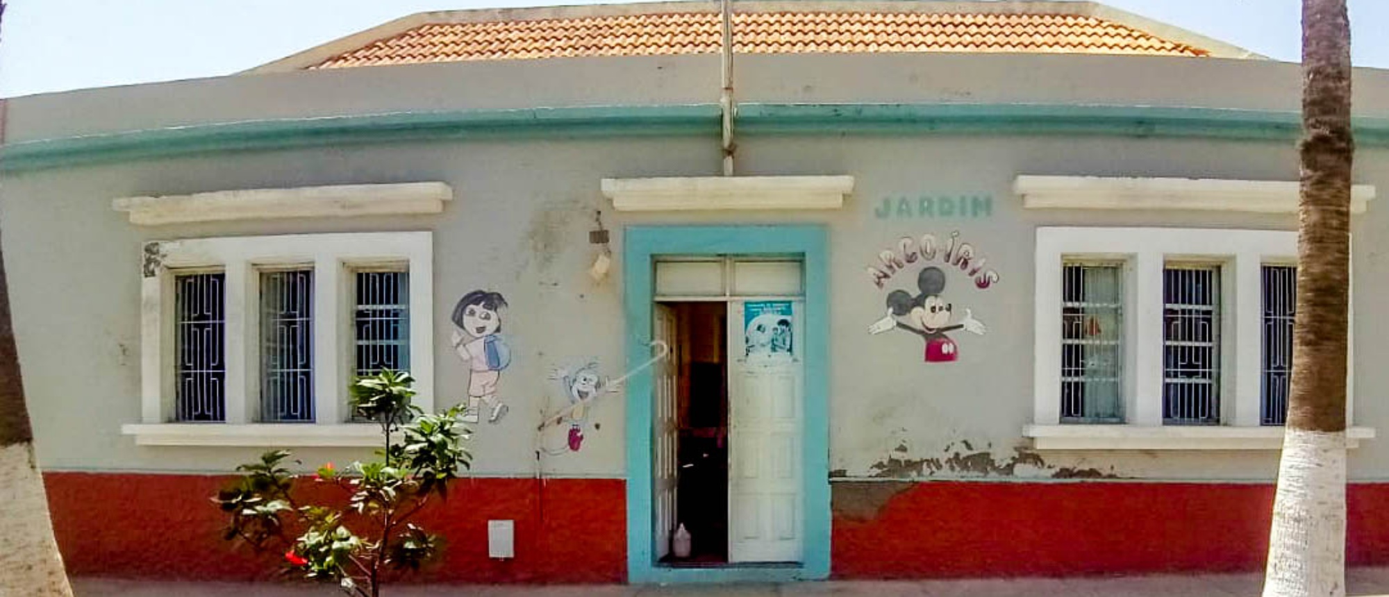 Colorful school building with cartoon murals, a blue door, and red base, awaiting renovation.