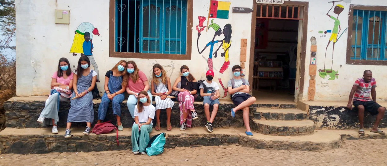 A group of masked volunteers sit on steps in front of a building with colorful murals.