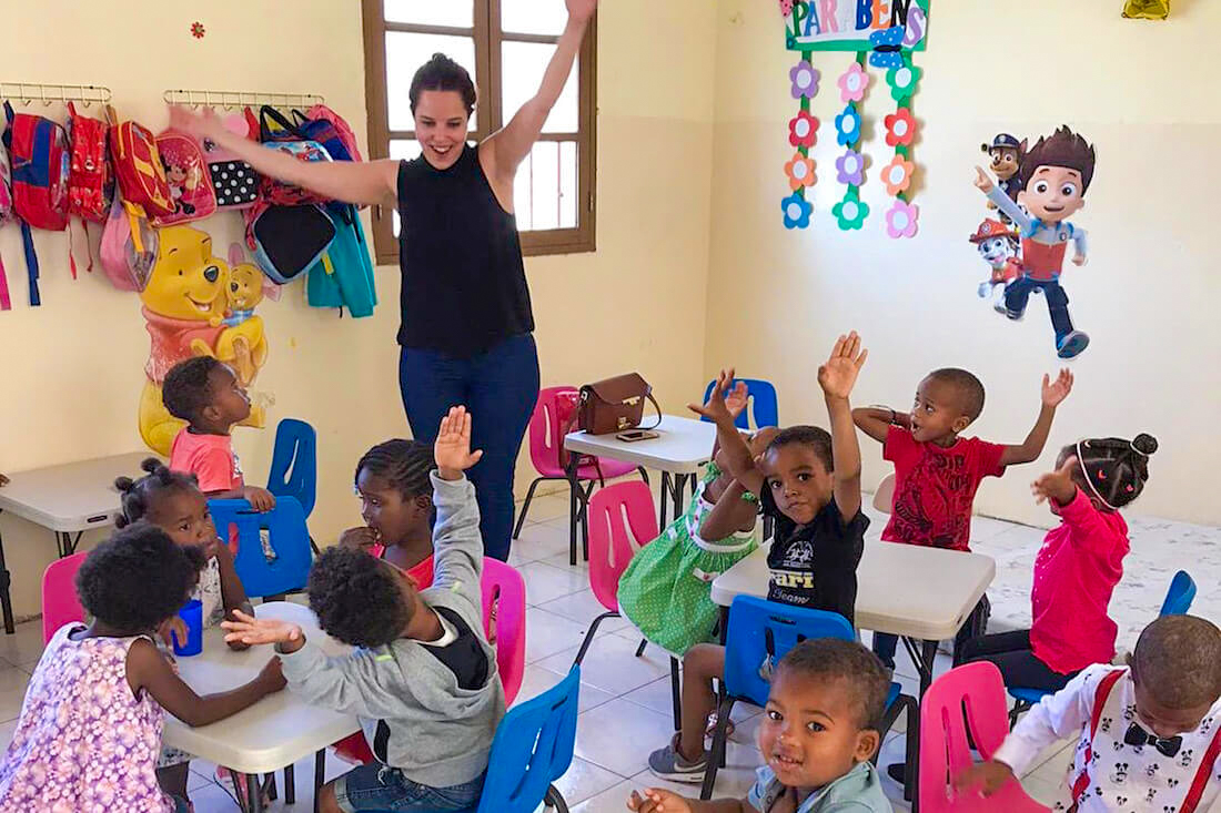 A volunteer teacher engages with happy children raising hands in a bright classroom in Cape Verde.