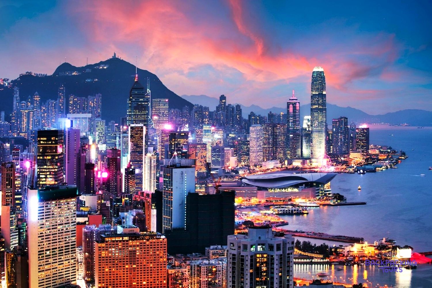 Hong Kong's skyscrapers glow pink and purple along the harbourfront beneath a fiery sunset sky.
