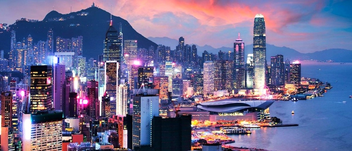 Hong Kong's skyscrapers glow pink and purple along the harbourfront beneath a fiery sunset sky.