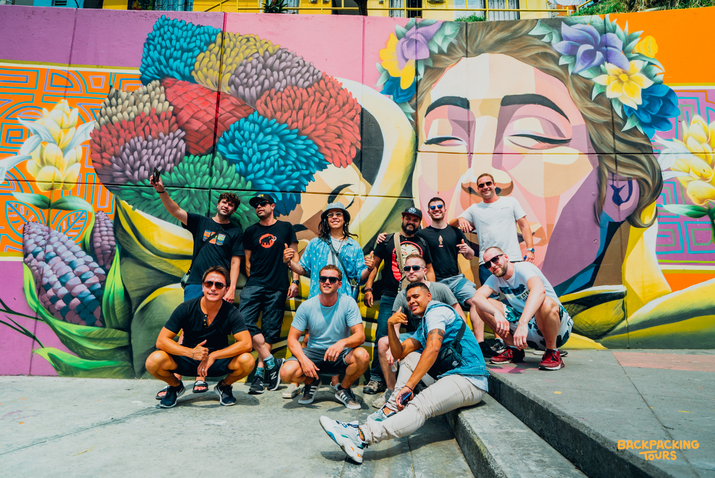 A group of happy backpackers posing in front of a vibrant street art mural in Medellín, Colombia.