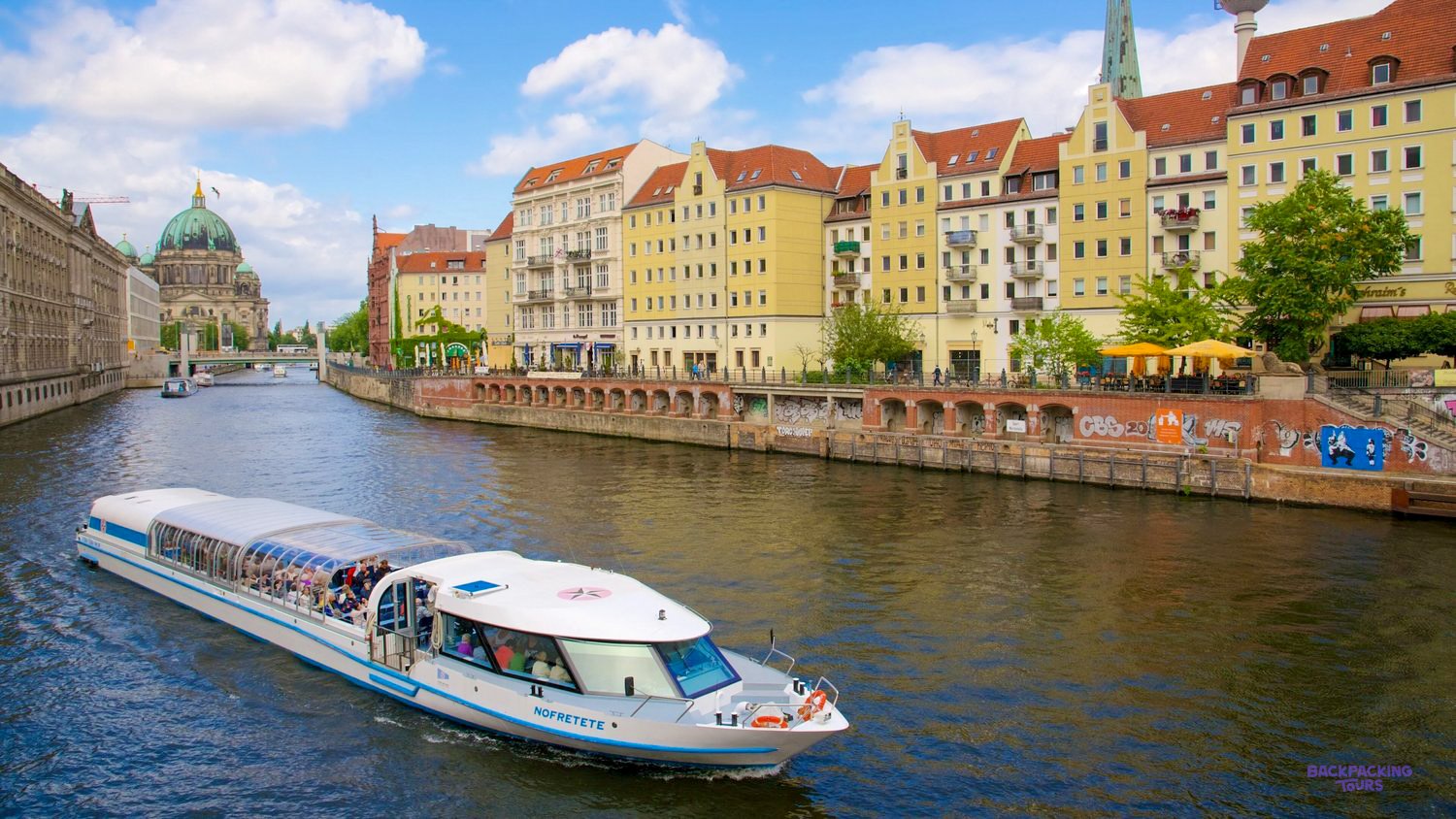 A sightseeing boat cruises the Spree in Berlin, past colourful buildings lining the riverbank.