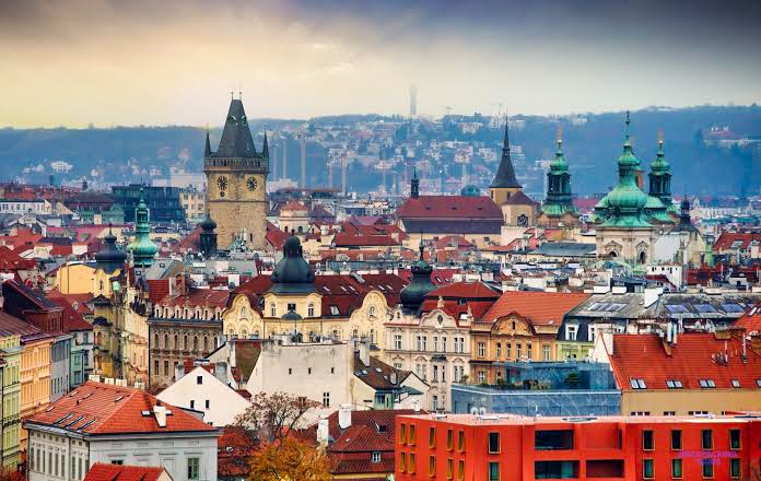 Red-roofed houses, a clock tower and green church domes spread across Prague towards the hills.