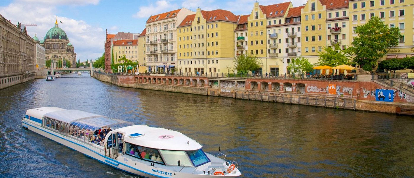 A sightseeing boat cruises the Spree in Berlin, past colourful buildings lining the riverbank.