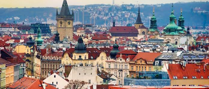 Red-roofed houses, a clock tower and green church domes spread across Prague towards the hills.