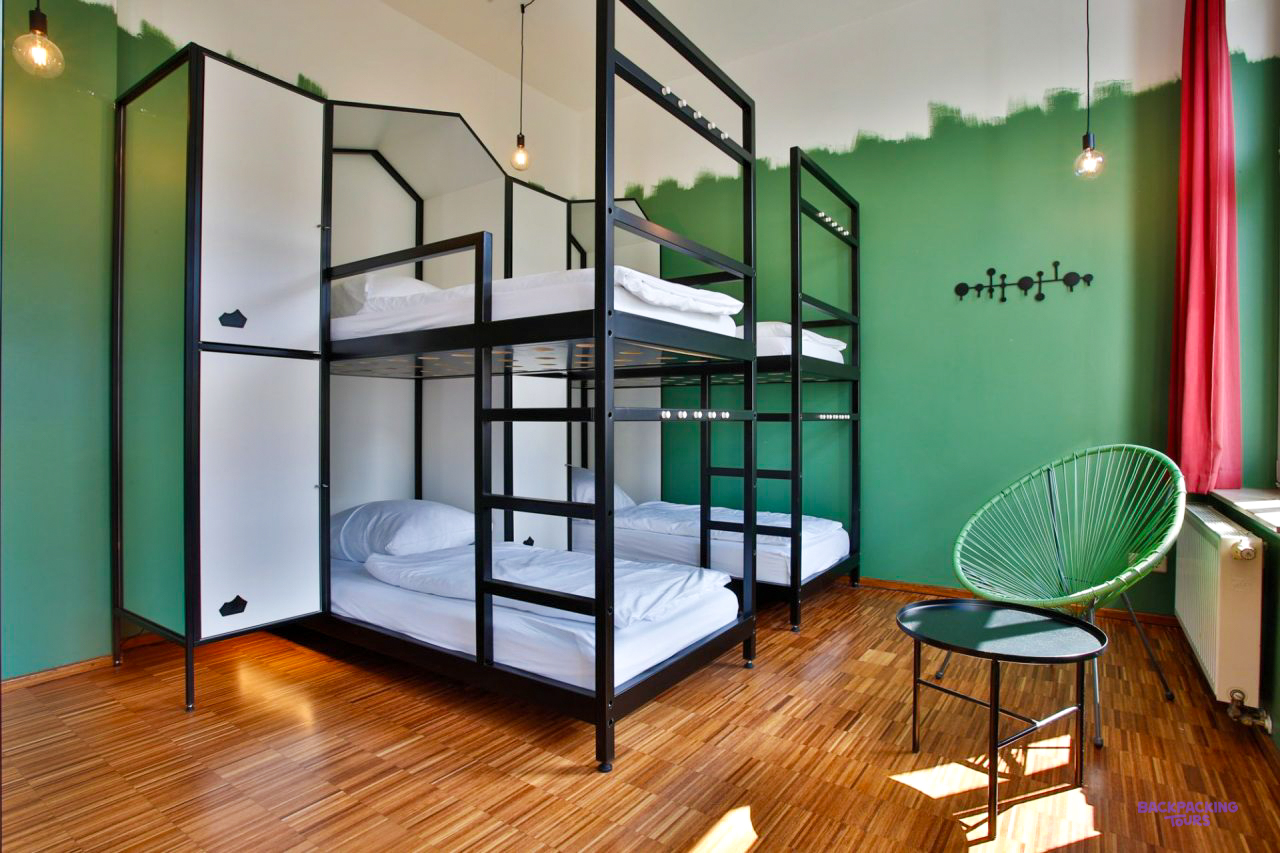 Black metal bunk beds and a green chair in a dorm room at the Berlin hostel