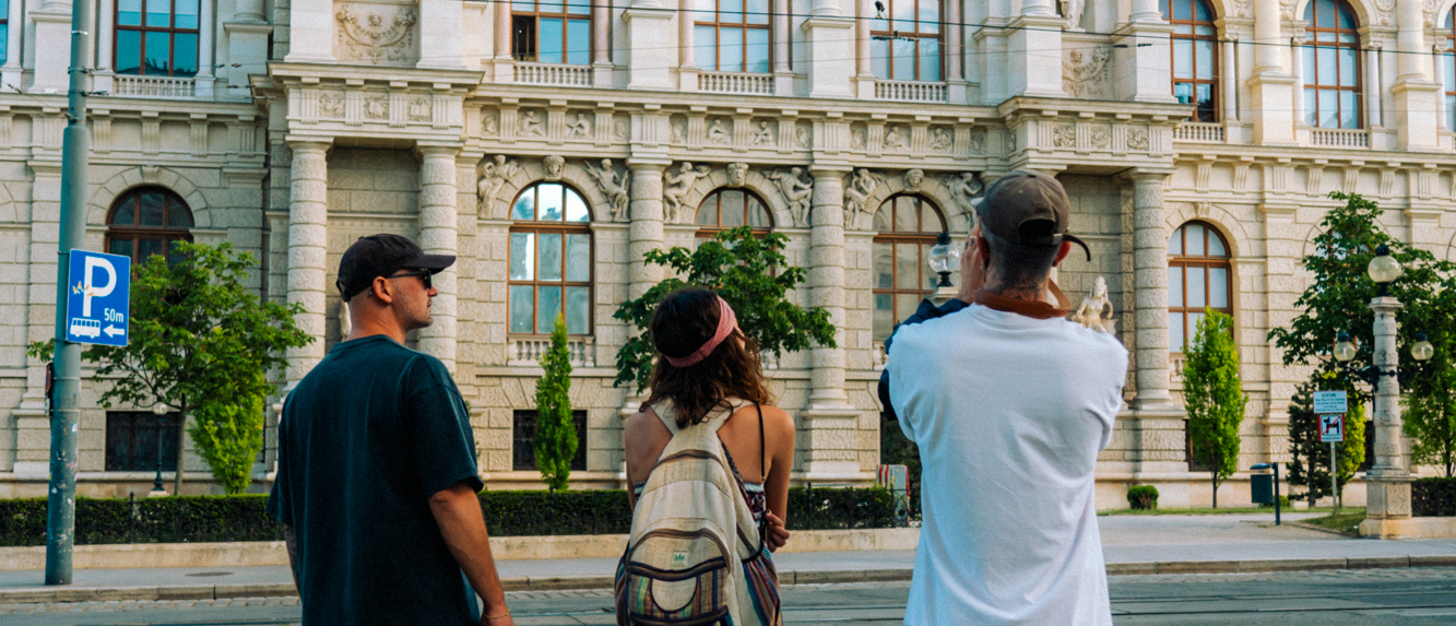 Three travellers stop to look up at an ornate building on a Vienna street.