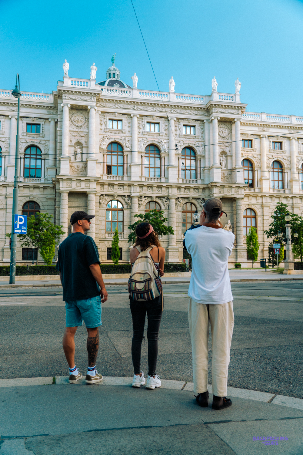 Three travellers stop to look up at an ornate building on a Vienna street.