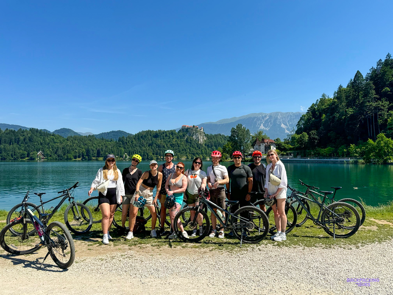 A group of cyclists stands with their bikes on the shore of Lake Bled.
