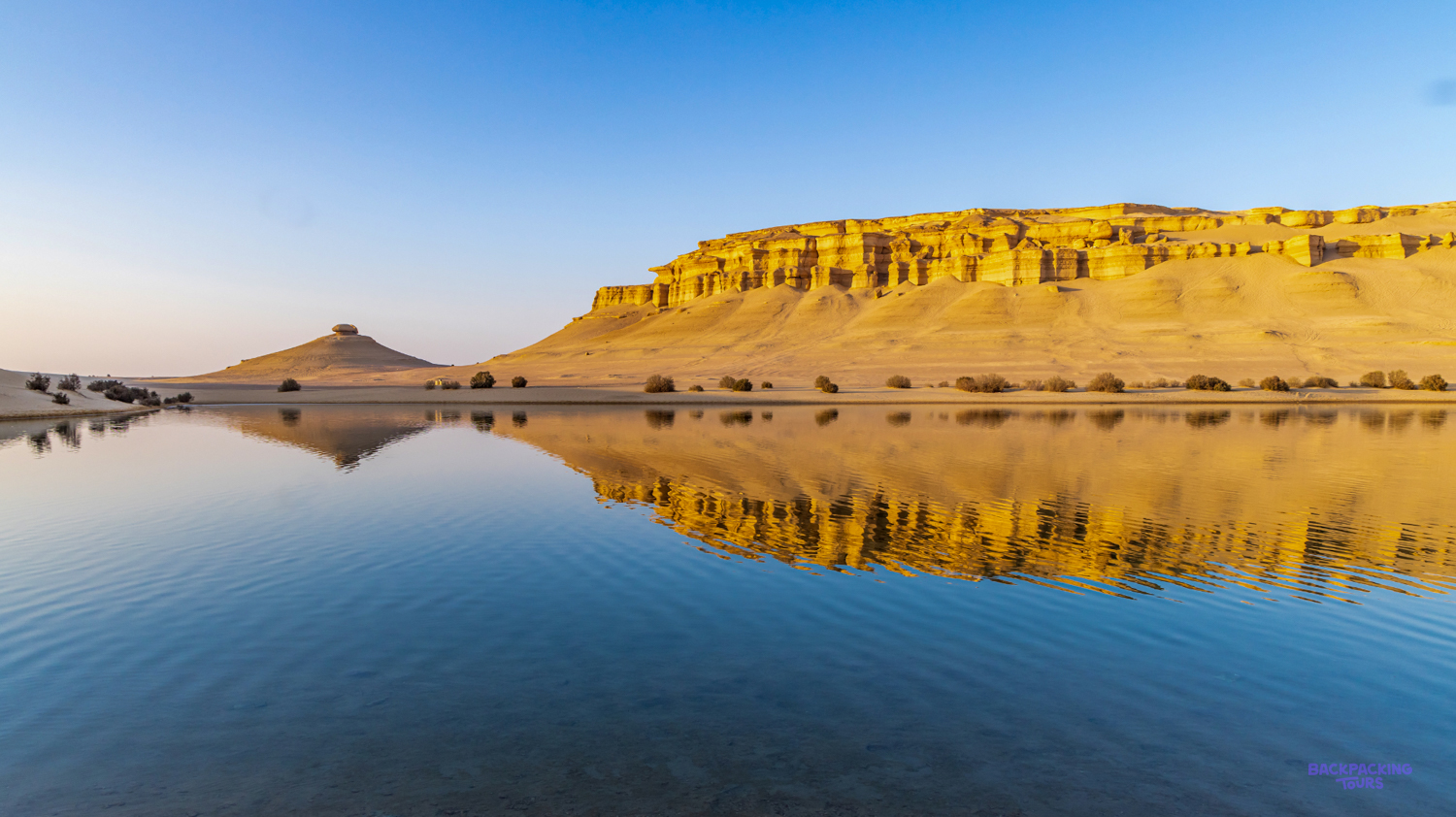 Golden desert cliffs and a clear sky beautifully reflect in the still waters of Faiyum.
