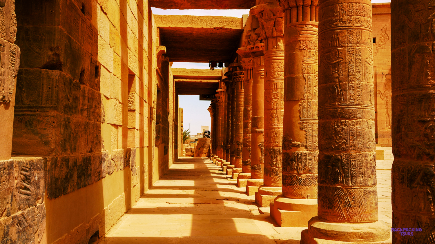 Warm light casts long shadows down a majestic corridor of Philae Temple in Aswan, Egypt.