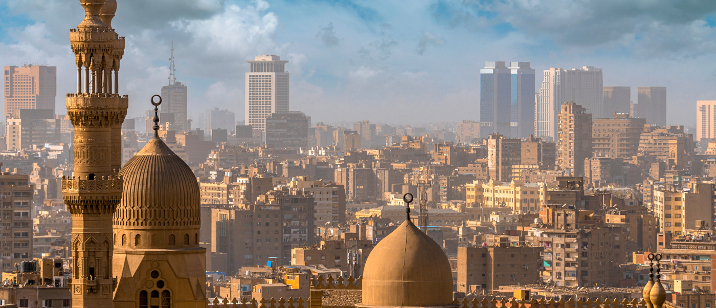 A panoramic view of Cairo's skyline, featuring historic mosque domes and modern high-rise buildings.
