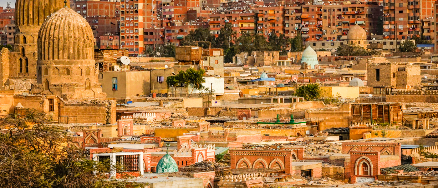A panoramic view of Cairo's historic cityscape, featuring many ancient domed buildings and densely packed structures.