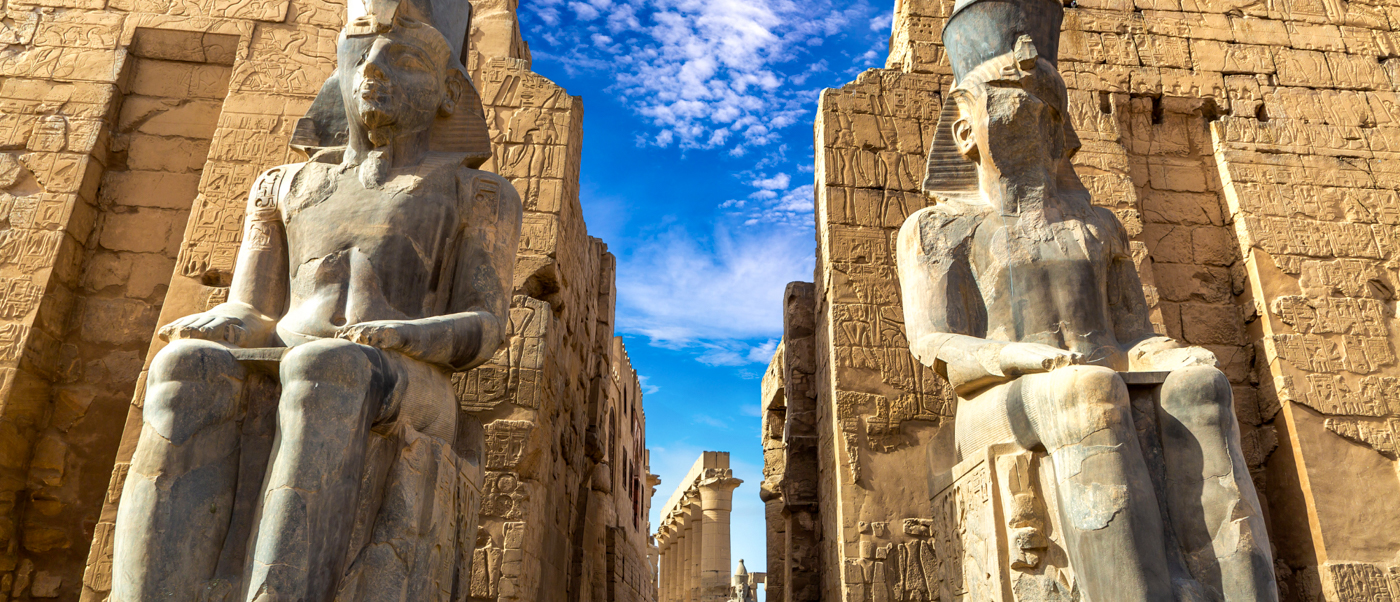 Two colossal seated pharaoh statues guard the entrance to an ancient temple in Luxor, Egypt.