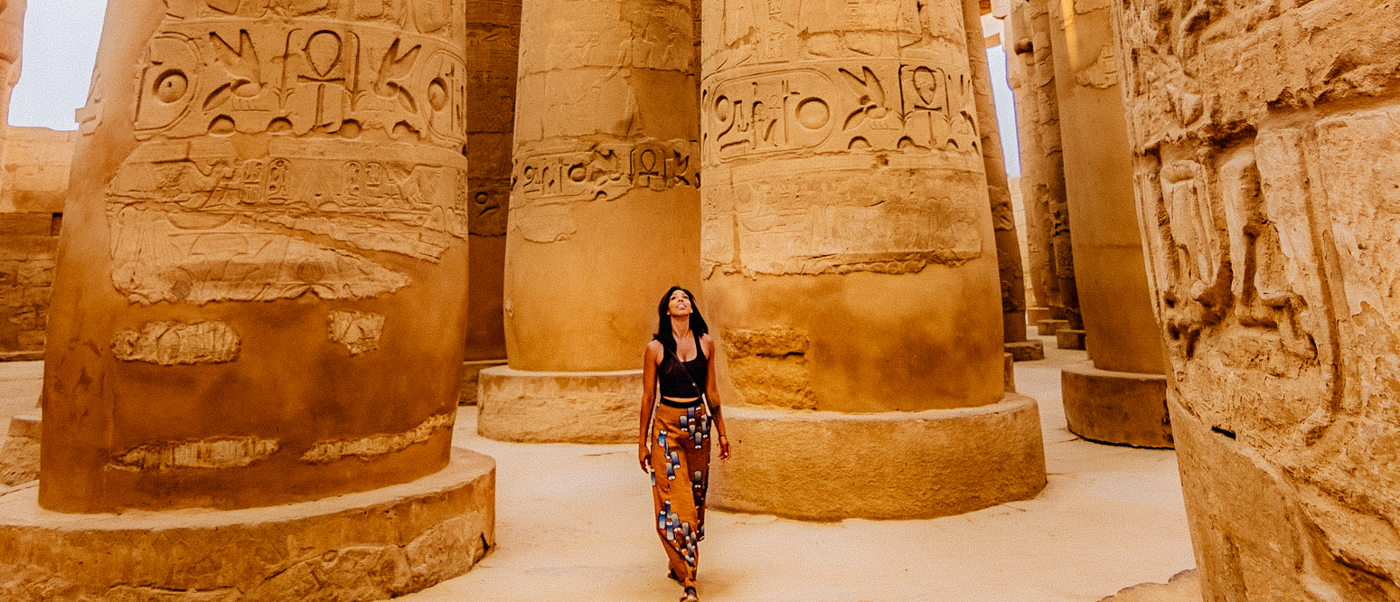 A woman walks through the grand, hieroglyph-covered columns of Karnak Temple in Luxor, Egypt.