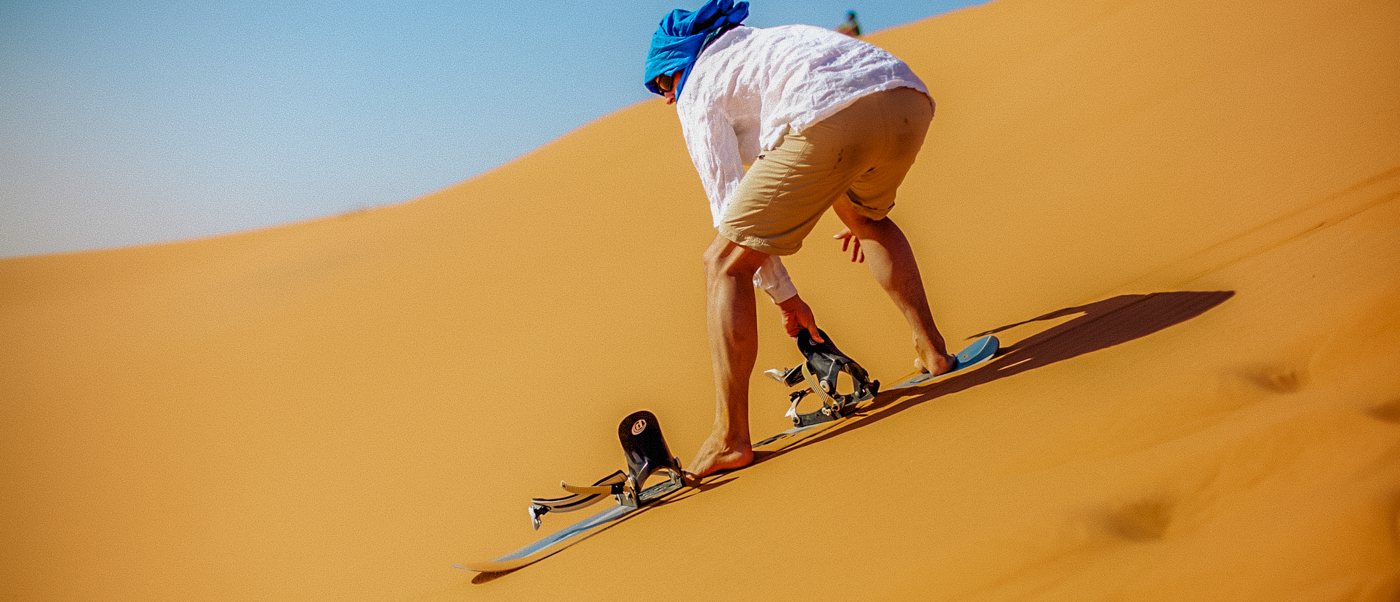 An adventurous person sandboarding down a vast golden dune in the Wadi al Hitan desert.