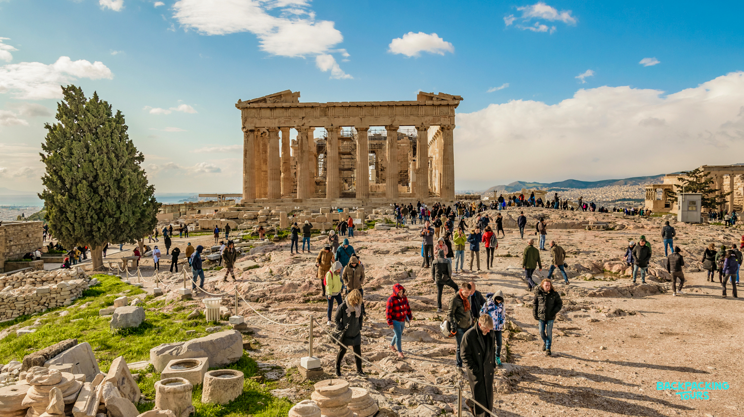Tourists explore the ancient Parthenon on the Acropolis in Athens under a sunny sky.