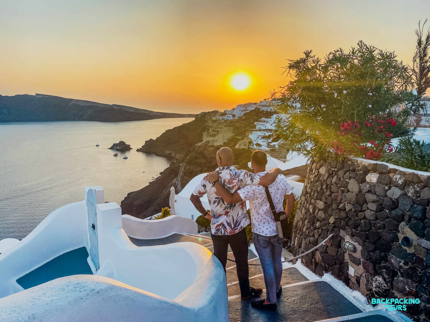 Two travelers share a moment, watching the spectacular sunset over the sea in Oia, Santorini.