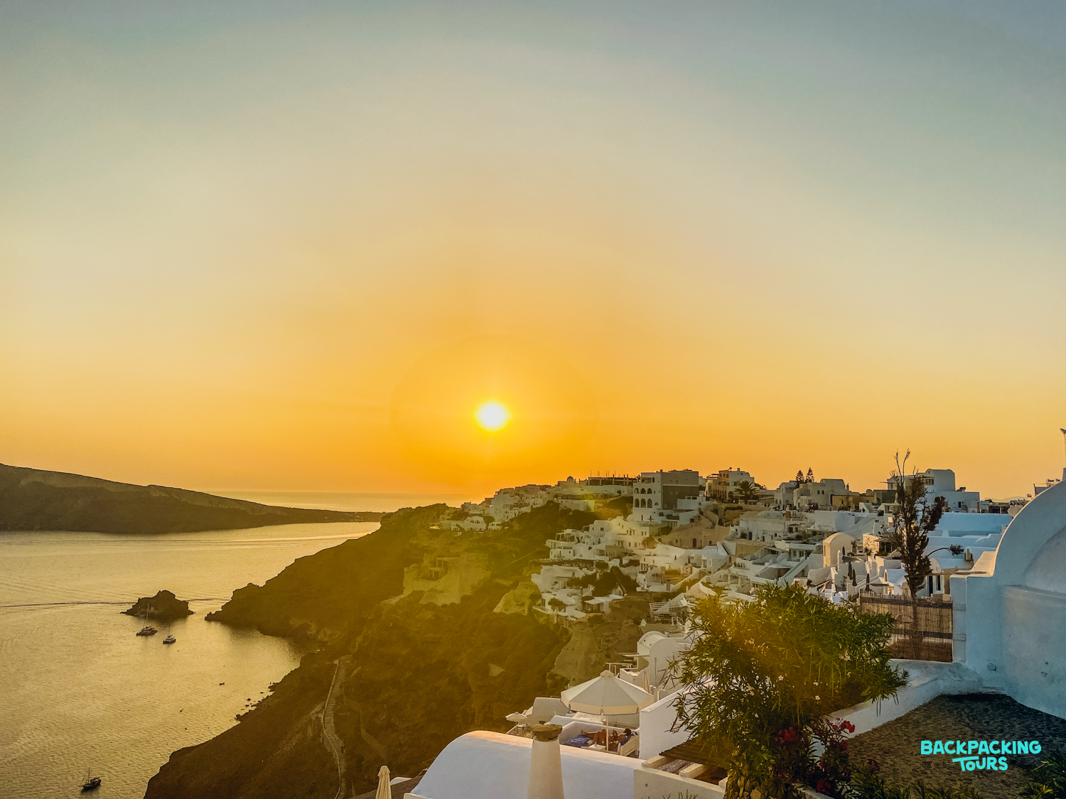A stunning golden sunset illuminates the white cliffside village of Oia, Santorini, by the sea.