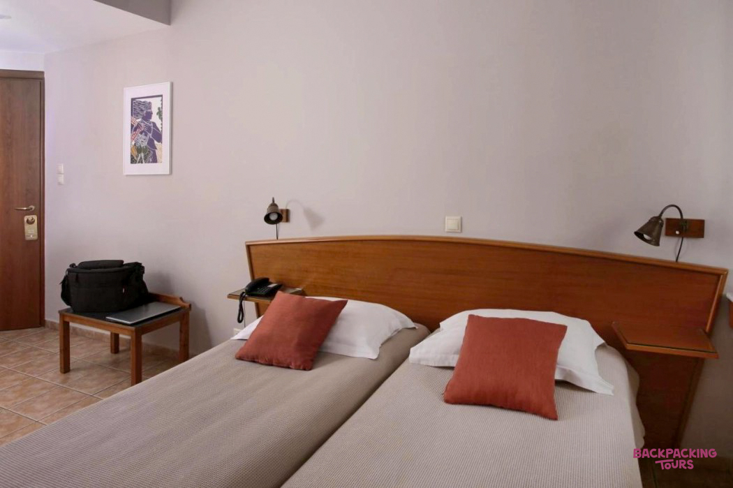 A comfortable hotel room with two single beds and warm lighting, ready for guests in Athens.