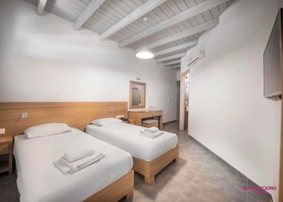 Comfortable twin room in Ios, Greece, featuring white beds, wooden furniture, and a beamed ceiling.