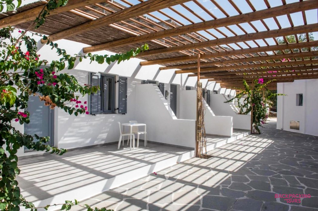 Sunny white Cycladic accommodation with private patios under a wooden pergola, perfect for relaxing in Ios.